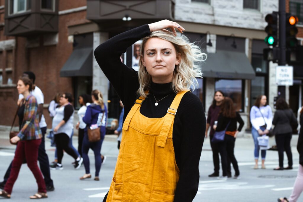 a woman in overalls on a street with people behind her